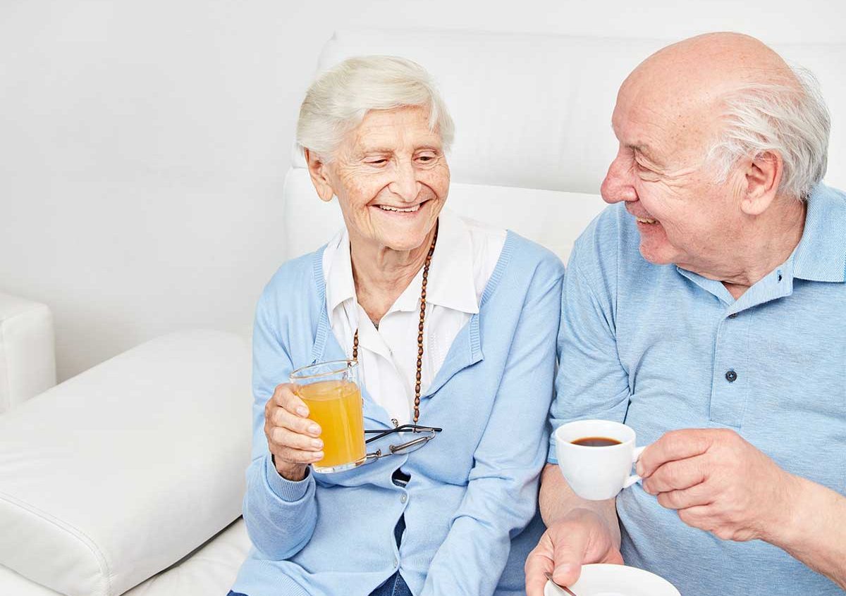 Happy, smiling senior couple sitting on the couch enjoying coffee and juice