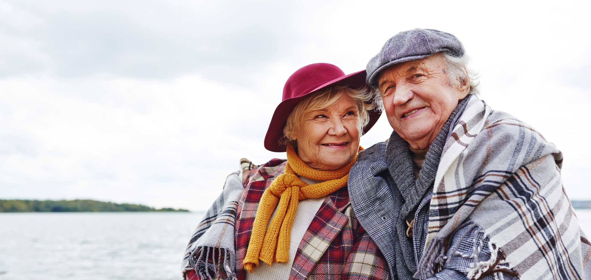 Happy Senior Couple cuddling under a blanket on the beach